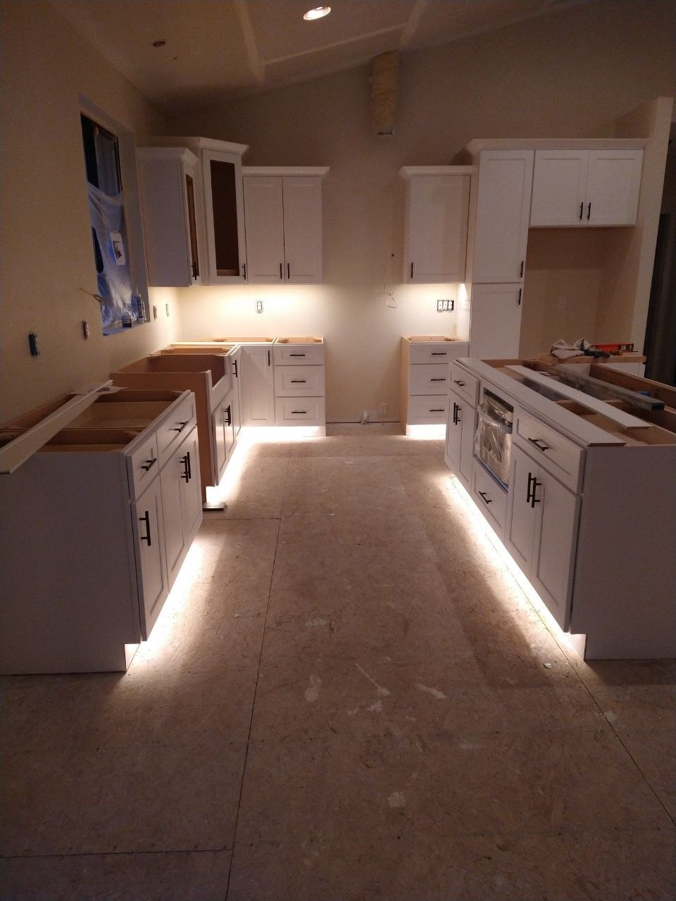 White kitchen with under-cabinet and toe-kick lighting before countertops and finishes are complete